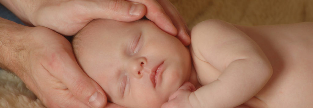 bébé allongé, tête entre les mains praticien reiki