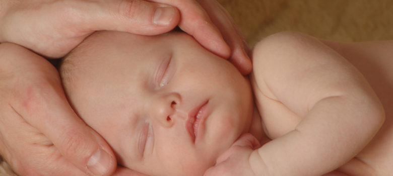 bébé allongé, tête entre les mains praticien reiki